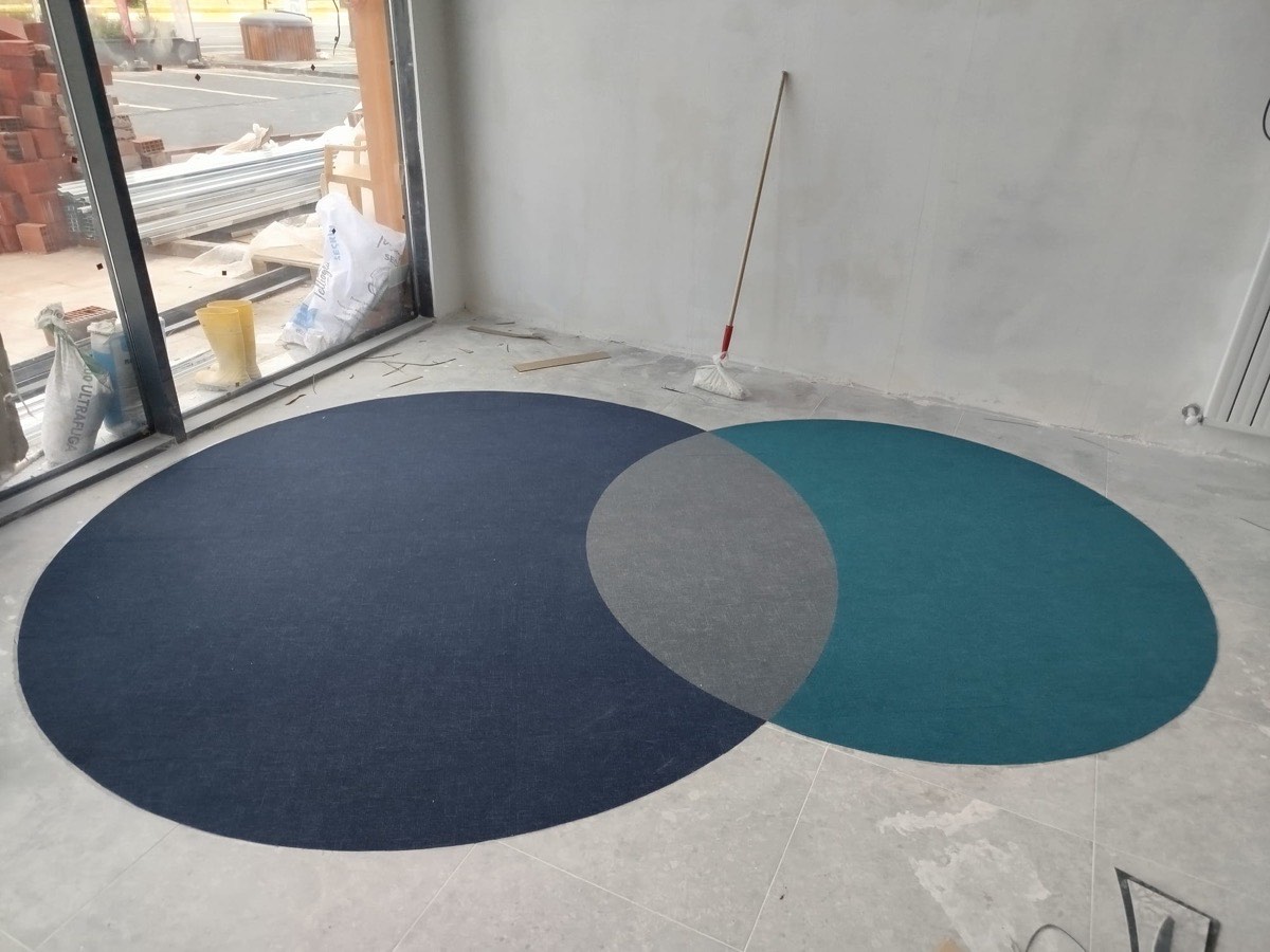Turkuaz ve lacivert daire desenli halı, cam cephe önünde